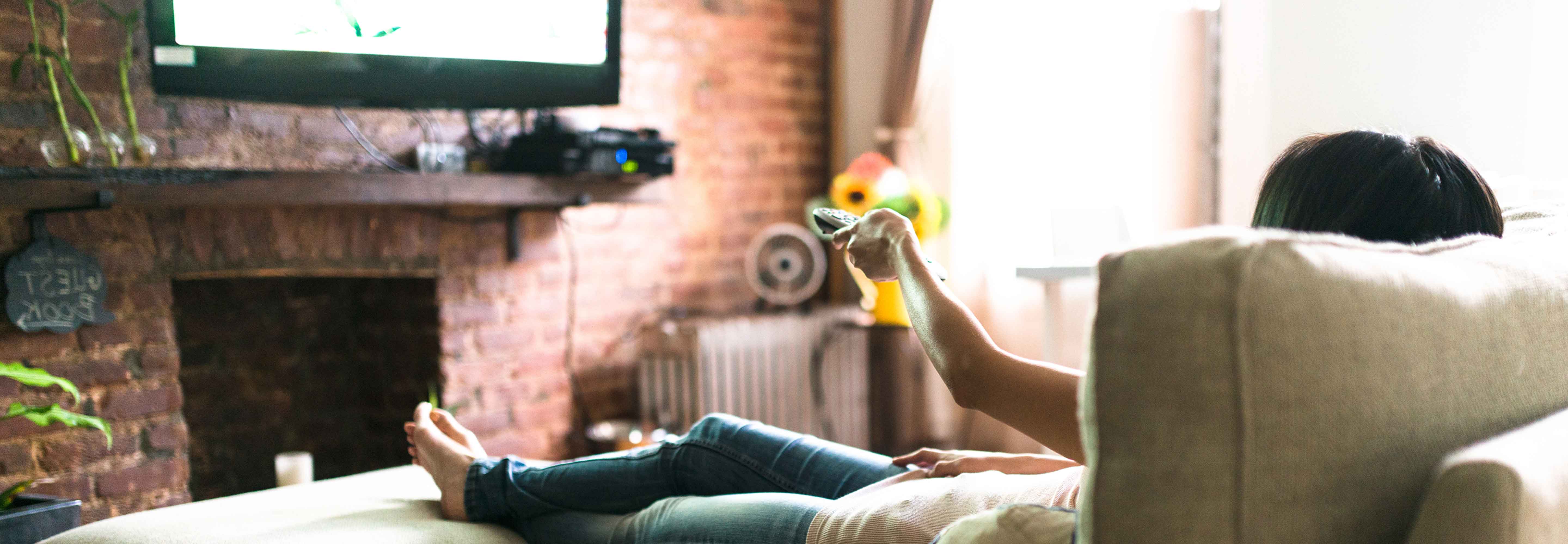 Woman on couch with remote control watching television