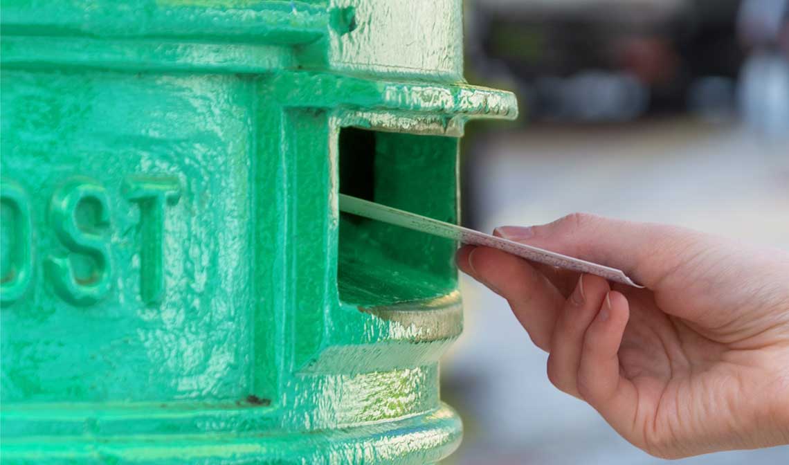 Persons hand, posting a postcard into a green pillarbox