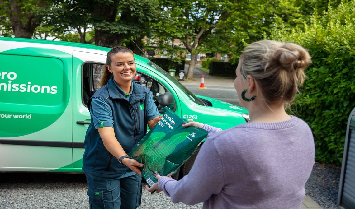 Male An Post operative standing beside a zero emissions van holding a parcel.