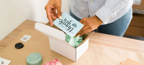 A business owner inserts a thank you card in a box for a customer order