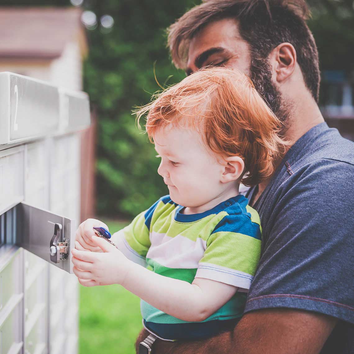 Man holding his son with keys standing at a set of communal postboxes outdoors