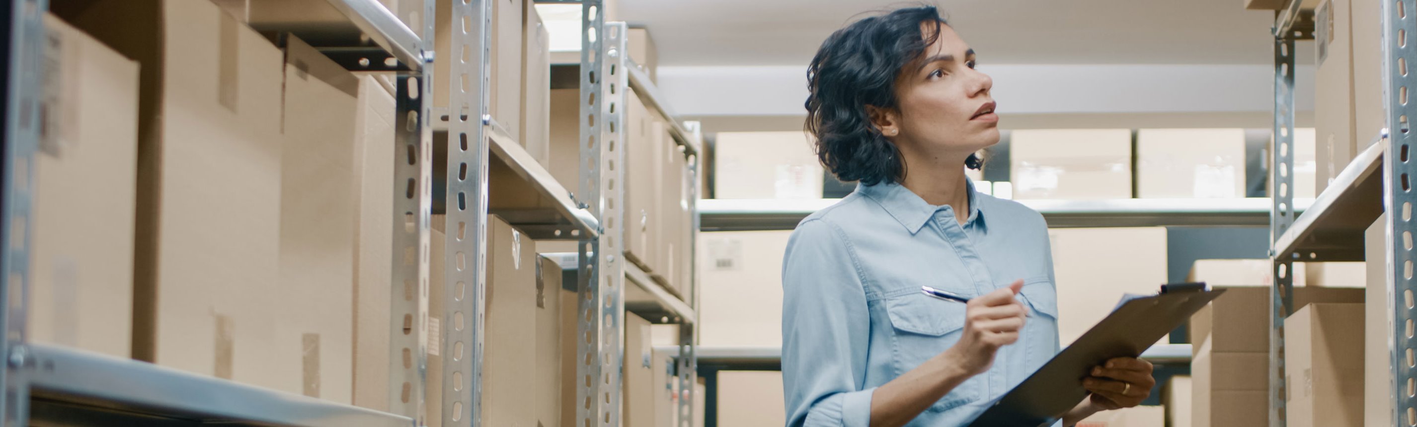 Female holding clipboard doing inventory in warehouse setting.