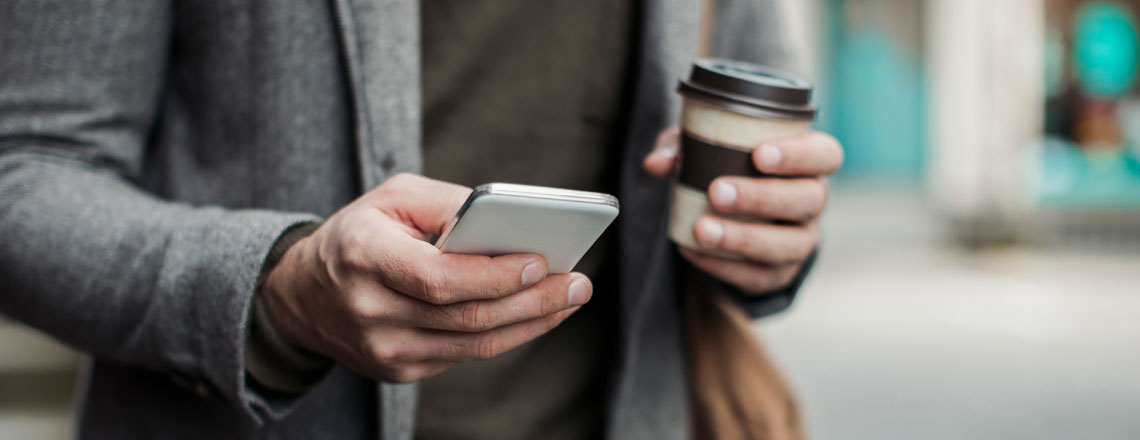 man holding a cup of coffee and searching on his phone on the go