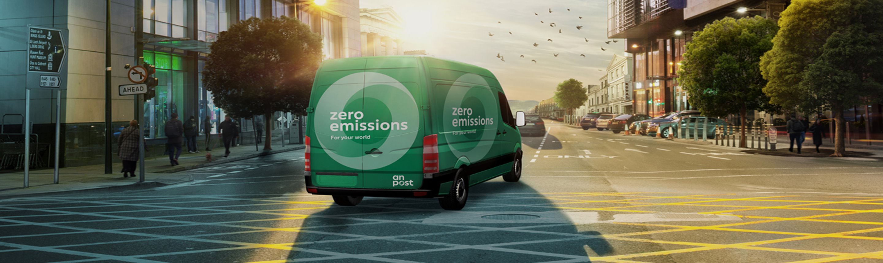 An Post zero emissions vehicle driving through urban street at sunrise.