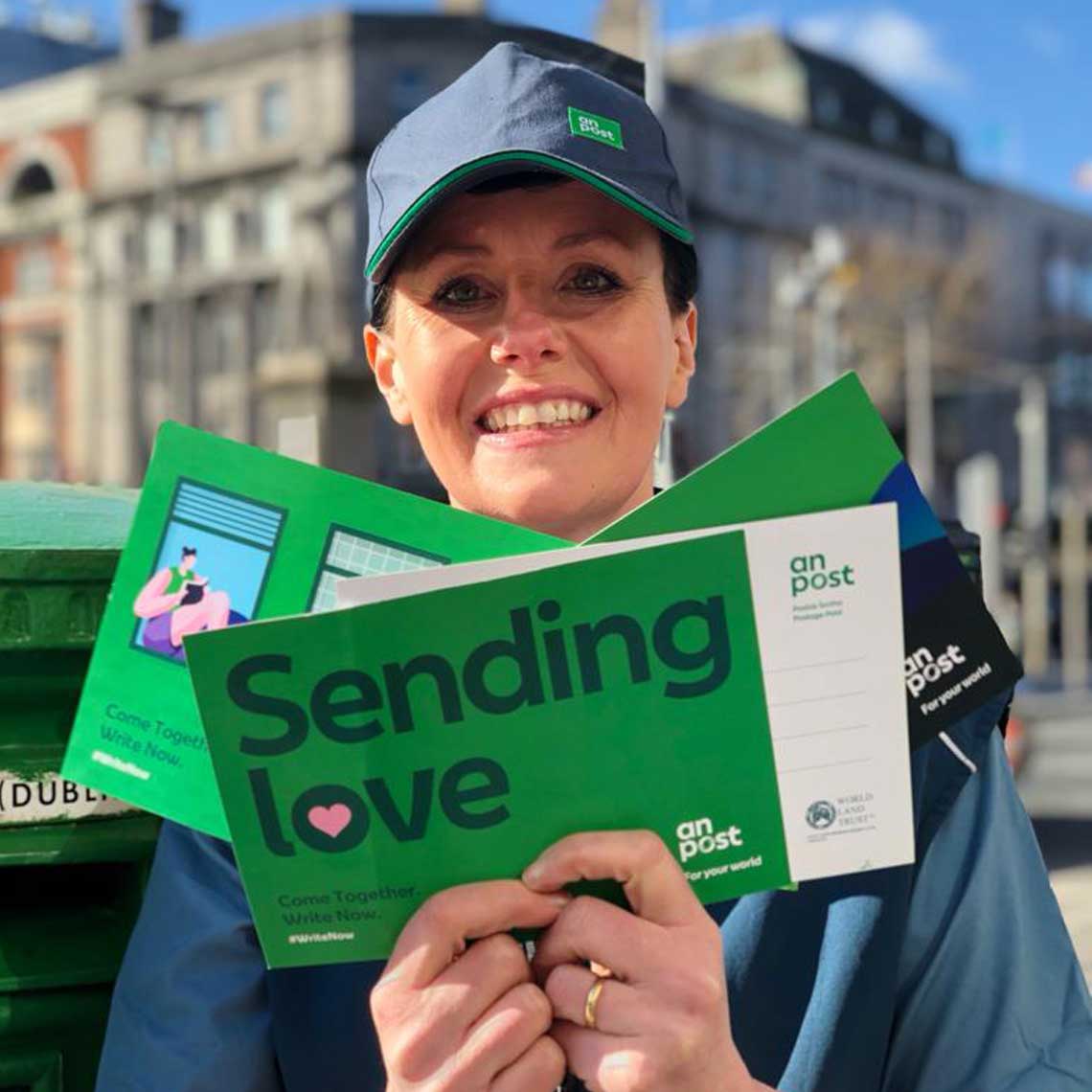 Postal operative holding a send love postcard standing in front of a postbox