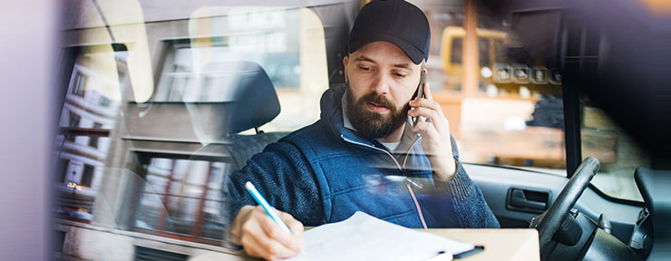 Delivery Man in van with parcel writing on clipboard